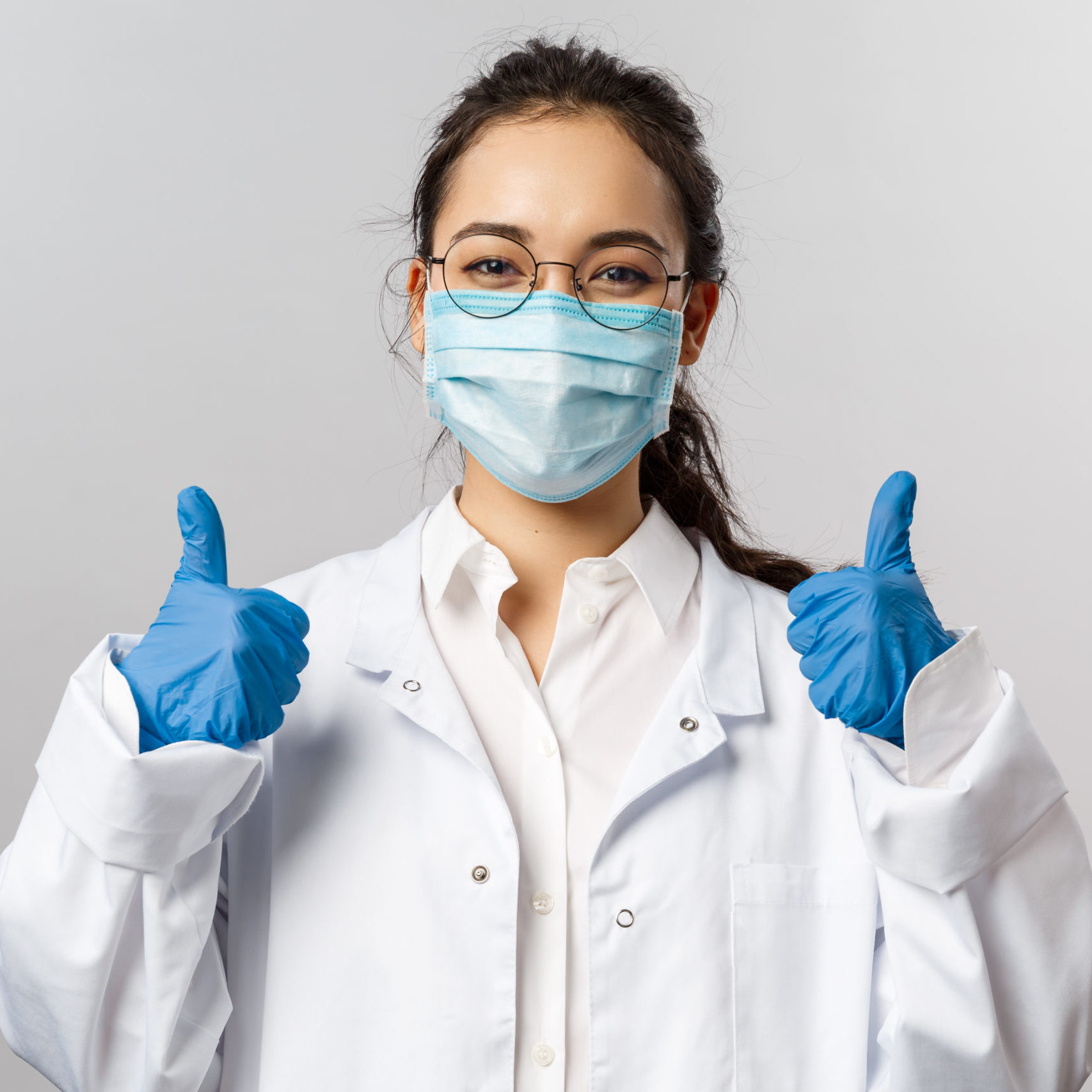 Doctors, infectionist, research and covid19 concept. Satisfied young asian female doctor receive good results on studying virus, discover vaccine, show thumb-up, wear face mask and gloves.